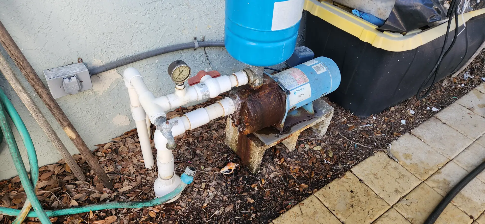 Irrigation pump and pressure tank plumbing on the side of a house